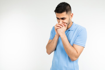Caucasian man in a blue T-shirt sincerely prays on a white isolated background with copy space