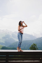 Naklejka premium A young beautiful girl in the mountains enjoys nature. The girl puts on sunglasses, smiles and enjoys a Sunny summer day.