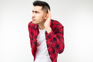 brunette man in a checkered shirt wide open eavesdrops on a conversation on a white studio...