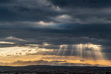 Panoramic view of dramatic sun ray through low clouds over city at sunset. The sun cuts through the clouds over the city. Sunbeams on the city