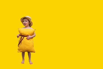 a beautiful little girl with a hat and a yellow pillow on her belly with a strap attached to her belt looks into the camera and smiles at a bright yellow background - a concept of orthopedic comfortab