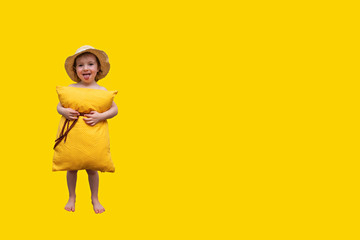 Little girl posing on a yellow background in a pillow instead of a dress and a straw hat. Pillow call. Vivid emotions: happiness, delight, sadness, tomfoolery. Happy childhood