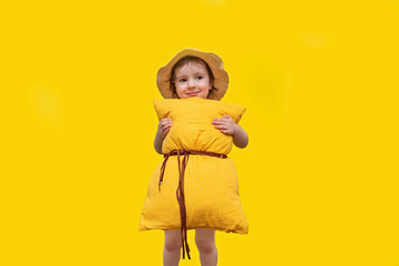 Little girl posing on a yellow background in a pillow instead of a dress and a straw hat. Pillow call. Vivid emotions: happiness, delight, sadness, tomfoolery. Happy childhood
