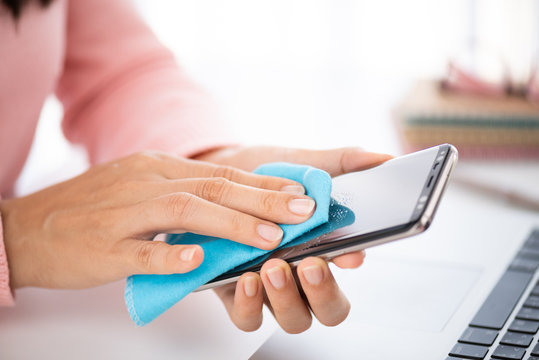 Closeup woman hands cleaning the smartphone screen with a fiber cloth from dirt dust and virus, against Coronavirus or Corona virus disease (Covid-19). Healthcare and disinfection concept.