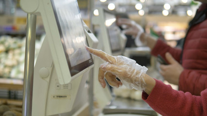 customer in plastic disposable gloves presses a finger on the touch screen of an electronic balance in a supermarket, a means of protection against coronavirus in a public place