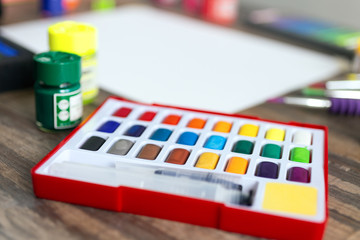 Multicolored watercolor set close up on wooden desk, art workplace
