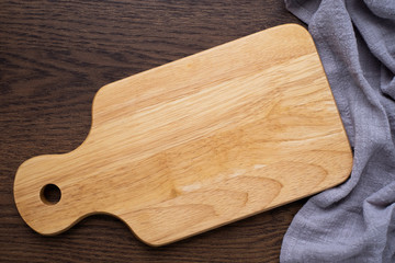 Top view above of Wooden chopping board with napkin on dark table background. Wood Cutting board with handle and hole for hanging. Empty utensil with copy space.