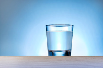 Drinking water against blue background. Glass of pure water on wooden table with copy space.