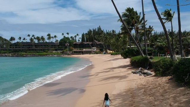 Flying over a girl walking on an empty beach in Maui