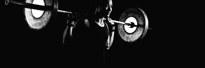 asian athletic strong man having workout and bodybuilding with barbells weight lifting backsquat style in gym and fitness center in dark tone black and white