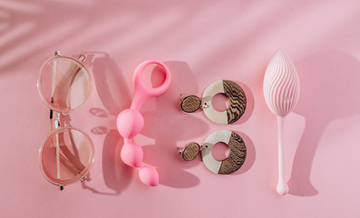 Summer female pink background with different sex toys, sunglasses, earrings and palm leaf shadow. Online store, shopping, delivery, Stay at home concept.