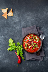 Mexican black bean tomato soup in clay bowl. Gray background