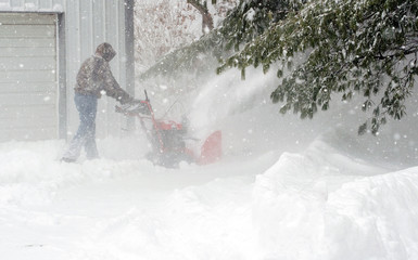 Working man is using a snow blower to clear snow in a residential area