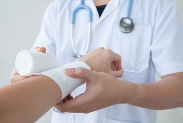 Doctor bandaging the wrist. Concept of first aids and treatment in wrist injuries. Closeup and selective focus on applying bandage onto patient's hand.