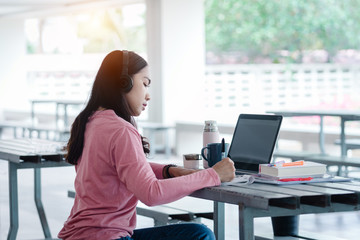 Portrait of a young Asian female adult learner studying online at home during Coronavirus or COVID-19  pandemic. Businesswoman work with laptop at home in house corridor and garden