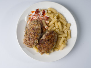 Meat cutlets with a side dish of penne rigate in a white round plate. Top view