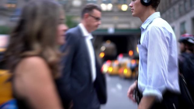 Slow motion effect of young businessman walking at crowd blurred street with anonymous hurry up people, Caucasian male in formal wear listening informative audio book via bluetooth headphones
