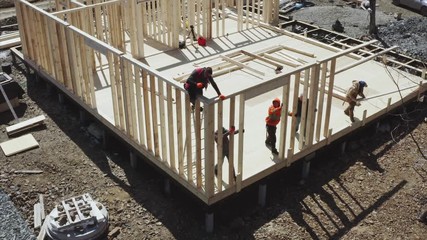 Aerial zooming out view of builder on the ladder jointing the wall with manual hammer. Frame house under construction