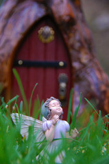 Sweet fairy statue stands in fairy garden surrounded by green grass. Fairy princess is in front of door to magical fantasy world. She is beautiful, mystical, and delicate.