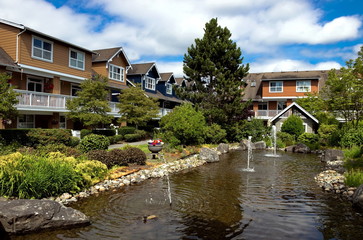 Fototapeta na wymiar Residential District in Richmond City, a village of townhouses with pond and fountain, green grass bushes and trees in the territory of residential complex, cloudy sky, Vancouver, British Columbia 