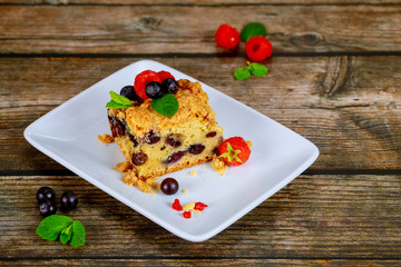 Piece of homemade blueberry coffee cake on white plate on wooden background.