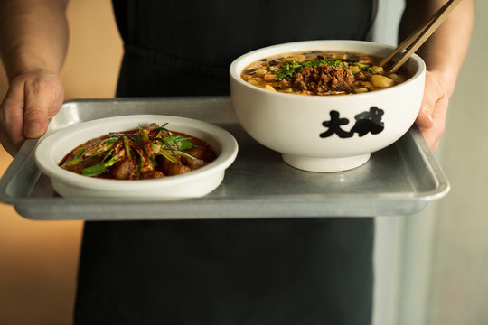 large bowls of noodles being brought out on tray by server