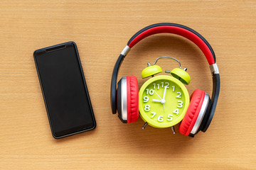 Headphones and alarm clock and smartphone on wooden desk. Musical concept