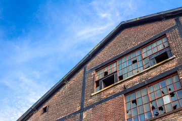 Fototapeta na wymiar Abandoned warehouse building, brick facade with broken windows, blue sky copy space, horizontal aspect
