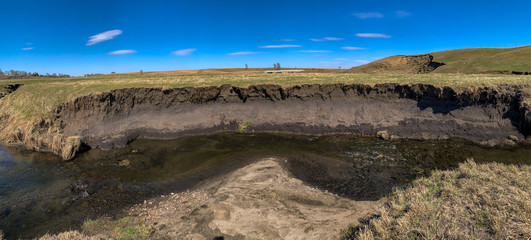 Soil erosion at drop off into a creek showing exposed roots and dirt along the water edge.
