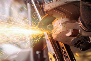 A young man welder grinder metal car an angle grinder   in the   workshop, sparks fly to the side