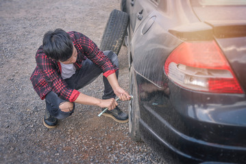 A young asian man is changing a tire.