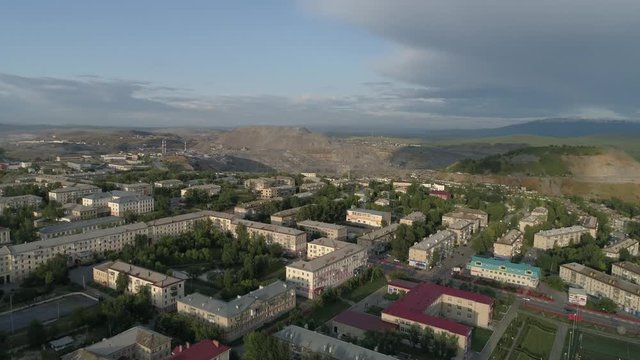 08. Aerial view of city with low buildings. The camera goes up and overlooks huge quarry and ore dumps. Outside the city Ural mountains. Summer, evening. Russia, Chelyabinsk region, Satka city
