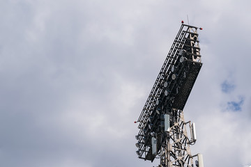 view of the tower for lighting stadiums, sports and concert areas, with searchlights and transmitting broadcasting antennas against a cloudy sky