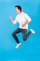 Young Asian man jumping with happy and excited over blue background