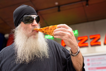 Mature bearded man eating New York style pepperoni pizza outdoors