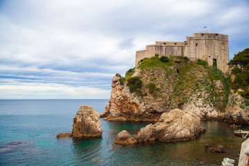 Fototapeta na wymiar Muralla de Dubrovnik en Croacia, con montaña y mar. Construida sobre la roca del mar Mediterraneo. Histórico pueblo turístico costero. 