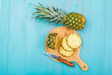 Fototapeta na wymiar Whole and sliced pineapple in a cutting board with a fruit knife top view on a blue cyan background