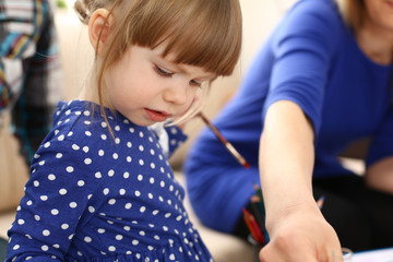 Blond smiling little girl hold in arm brush drawing something together with mom. Beautiful female...