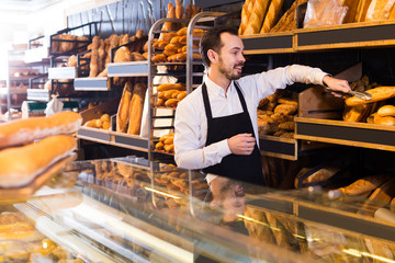 Fototapeta na wymiar Male shop assistant demonstrating delicious loaves of bread in bakery