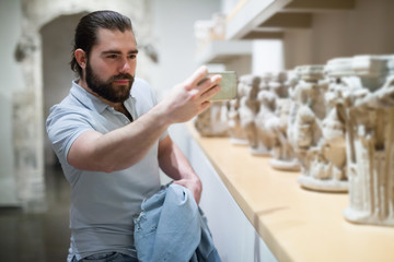 Adult male visitor using phone in sculptures exposition at museum