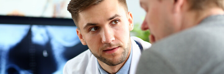 Portrait of serious doc indicating diagnosis to man. Physician wearing white uniform and stethoscope. Medical treatment and health care concept. Blurred background