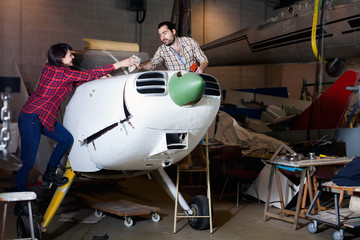 Two young mechanics, man and woman, repairing light sport plane in workshop