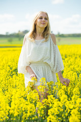 Naklejka na ściany i meble Girl posing in rape seed flowers field posing in white dress at sunny day