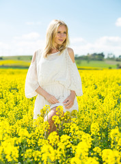 Young female posing  in yellow oilseed rape  field wearing in white dress