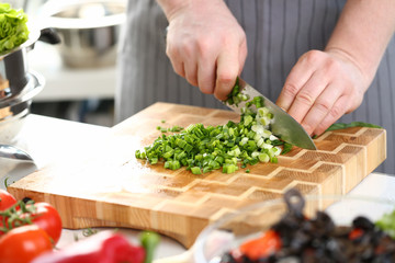 Male hand cook hold knife and cut green onion concept against kitchen background