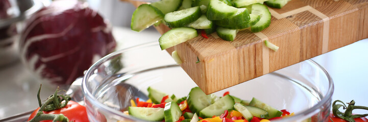 Green Chopped Cucumber Slices Pouring Glass Bowl. Healthy Dieting Salad Ingredient. Fresh Organic Vegetable. Hot Chili Pepper and Small Cuke Pieces. Vegetarian Kitchen. Horizontal View Photography