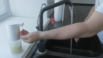 Man washes hands with soap in the kitchen with brush