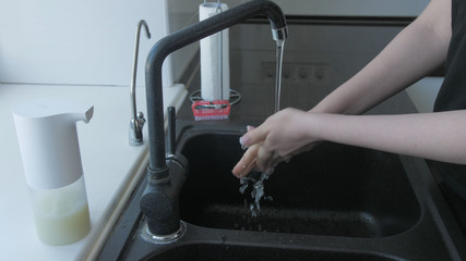 Woman washes hands with soap in the kitchen with brush