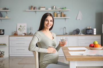 Beautiful pregnant woman drinking water in kitchen