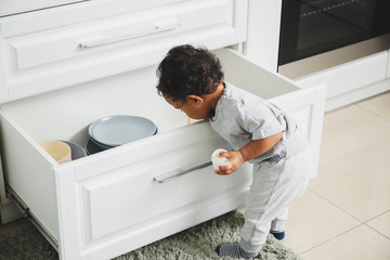 Little African-American baby playing in kitchen. Child in danger